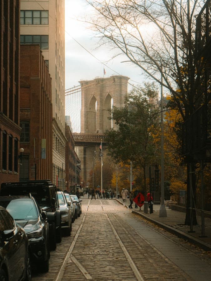 Cobblestone street with autumn trees leading toward the Brooklyn Bridge tower