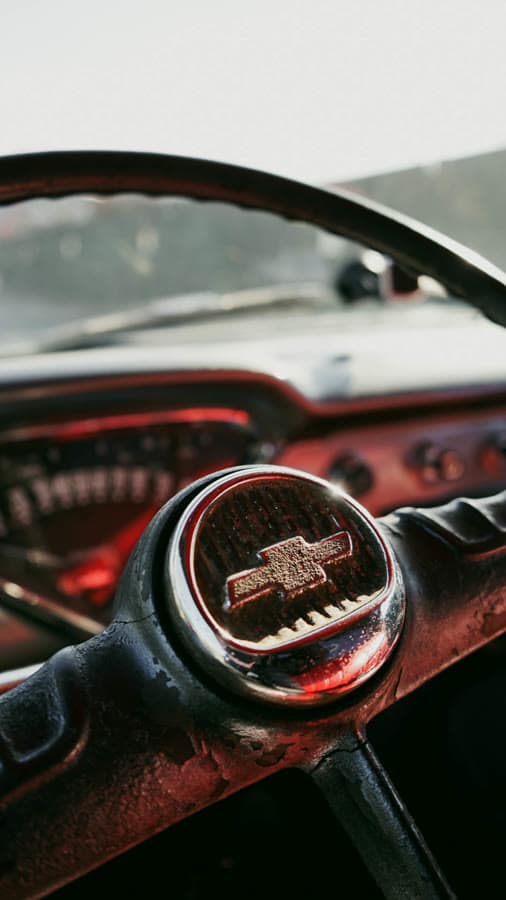 Close-up of a vintage truck's red steering wheel and horn badge